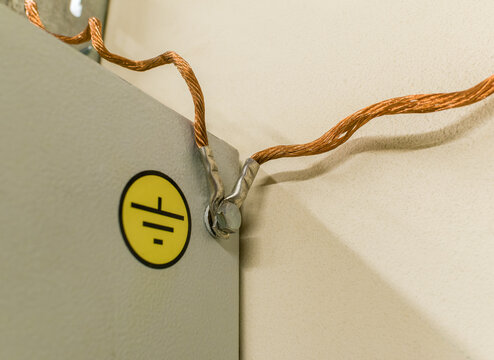 A copper multi-strand grounding wire screwed with a nut to a metal cabinet with a yellow "Grounding" label