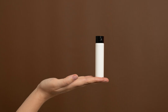 Hand holding white cosmetic bottle, brown background