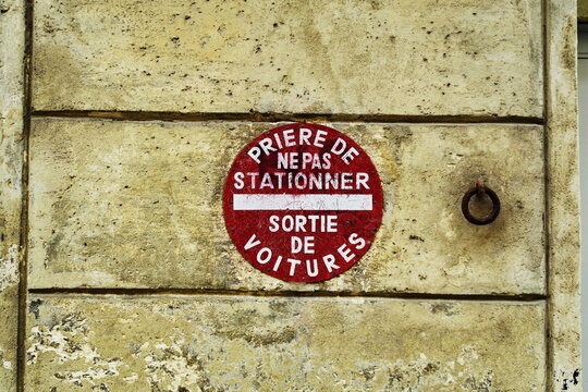 Pri&egrave;re de ne pas stationner. Sortie de voiture. Inscription sur panneau rond rouge et blanc de sens interdit sur mur de pierre.