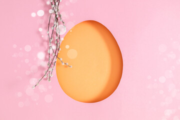  Easter background featuring a silhouette of a large orange paper egg on a soft pink background with bokeh highlights, complemented by willow branches in a flat lay.