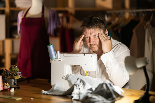 Tired male tailor rubs temples, tiring days work is behind him