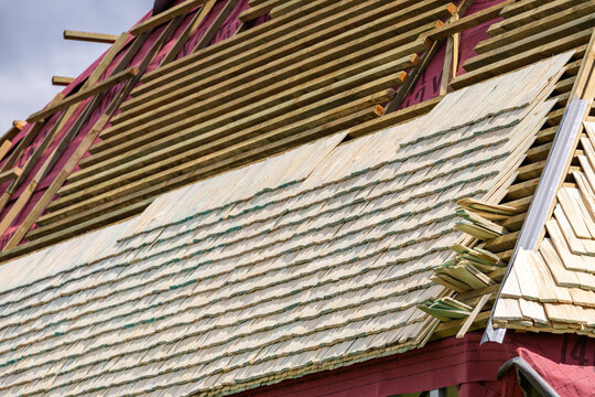 Construction of a wooden shingle (shake, shingle, or shindel) roof. The image shows the process of installing natural larch or aspen wood tiles on the roof battens. Roof truss system.