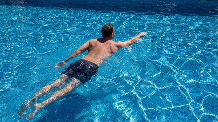 A man enjoys a refreshing swim in a clear blue swimming pool on a sunny day, showcasing a healthy and active lifestyle