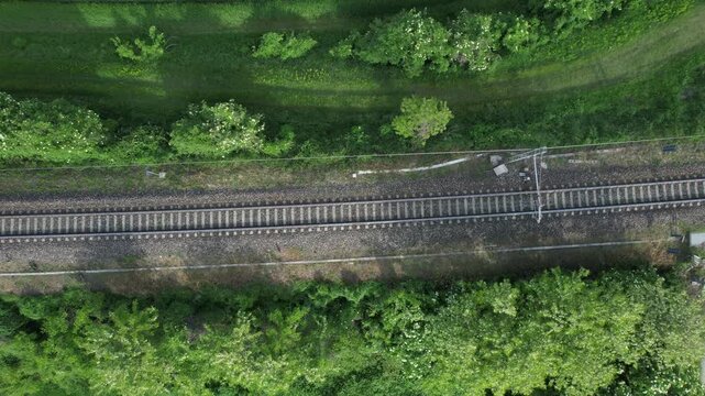 Drone top down ascent over parallel railway tracks and a rural road crossing through green countryside with trees, fields, and transport infrastructure.