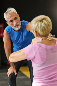 Senior mature woman exercising at gym, portrait of a mid aged trainer or coach talking to inured senior woman, suffering a back pain, neck pain, support and advice