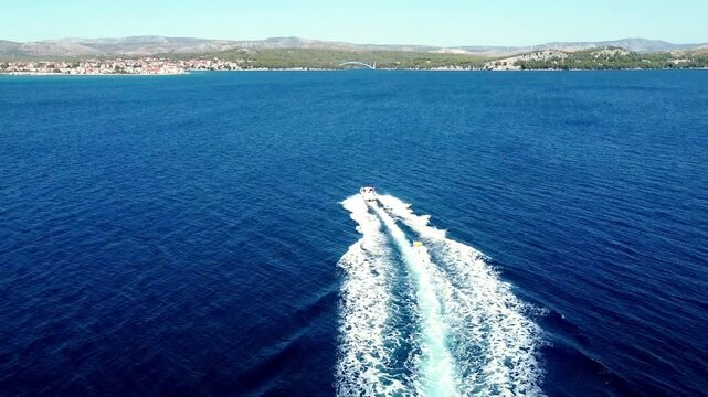 Top down aerial of speedboat leaving white wake across deep blue sea with tube pulled behind, static