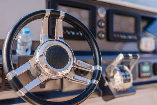 Yacht steering wheel with chrome finish and control panel, featuring gauges and buttons, positioned in a modern boat cockpit setting