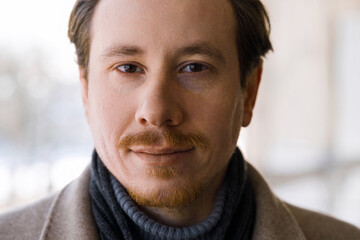 Fototapeta premium Close-up portrait of an attractive young redhead caucasian man wearing a coat on a cold, snowy winter day while walking down the street.