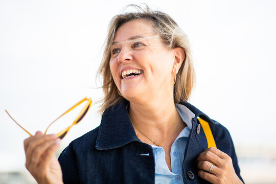 Smiling mature woman enjoying sunny day while holding sunglasses