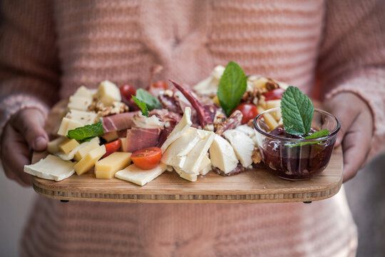 Close-up of a teenage Girl holding a wooden chopping board with assorted cheese and cured meat antipasto 