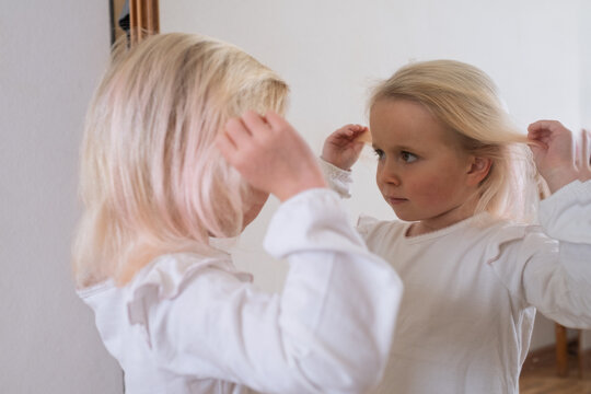 Cute little blonde girl admiring herself in the mirror.