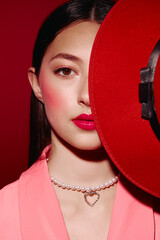 Fashion creative portrait of woman with red hat half covering face, striking pink lip makeup and...