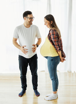 Happy young couple bonding, pregnent woman, father having fun both holding stomach at home