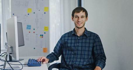 Portrait confident smiling male programmer working with robotics code AI software and looking at camera in tech office. Artificial intelligence dashboard, robotics, user interface, machine learning.