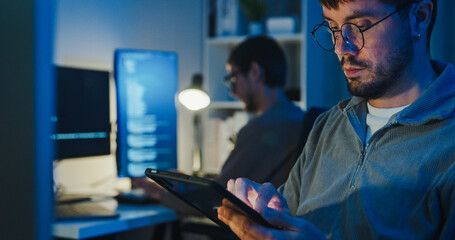 Team adult male freelance developer work late use tablet write prompt AI bot app program nomad terminal code at office night. Artificial intelligence dashboard, robotics, interface, machine learning.