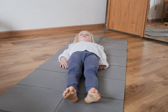 Little girl practicing yoga, lying in Savasana Corpse Pose on a mat.