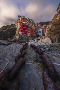 View of rustic chains leading the eye towards the colorful buildings nestled into the cliffs along the coast, Riomaggiore, Liguria, Italy.