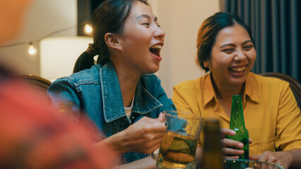 Group of multiethnic adult Asia friend drink alcohol beer bottle glass and fun talk laugh enjoy hangout party at dining table in night life indoor home. Happy hour millennial generation inside house.