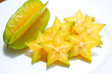 Fototapeta premium Sliced star fruit or carambola on white plate. Fresh tropical yellow fruit slices in star shape.