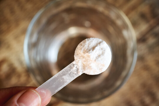 A scoop of L-glutamine powder above a glass of water. Amino acid for gut health..