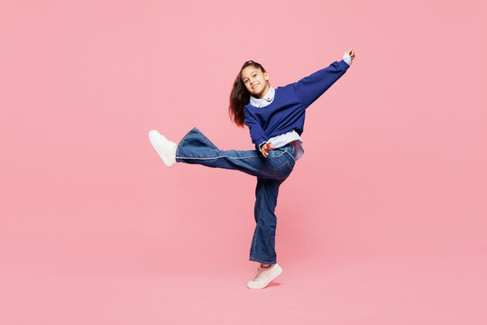 Full body side view little kid girl 8-9 years old she wears blue shirt have fun dance raise up leg isolated on pink color background child studio portrait. Mother's Day love family lifestyle concept.