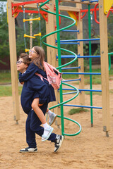 Fototapeta premium A boy gives a girl a piggyback ride on the playground, both smiling in school uniforms, radiating joy, trust, and playful friendship during recess.