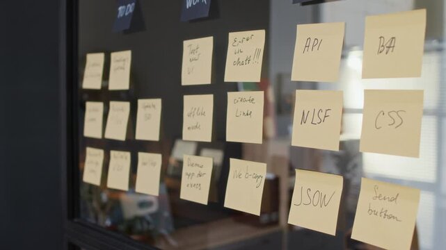 No people tilt-down shot of handwritten sticky notes for tracking progress on glass panel in organized modern office workspace