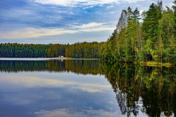Fototapeta premium Serene Lake with Forest Reflections Under a Cloudy Sky