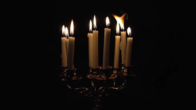 Elegant silver candelabra with lit white candles against a stark, dramatic black background.