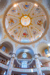 Naklejka premium Frauenkirche in Dresden shows its dome and detailed design. Visitors admire the artwork on the ceiling while exploring the church's space and structure. Light enters through the windows.