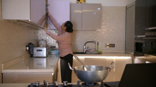 A beautiful housewife cooking food in the kitchen - Watching cooking recipes on a laptop  modern mother  . An Indian woman in her thirties is busy working in her modular kitchen - an Indian househo...