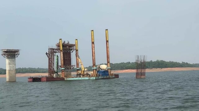 Unrecognizable workers atop bridge pillar under construction. Real time during ferry trip
