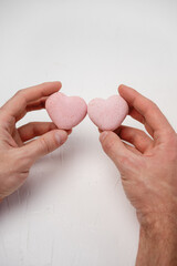 Hands of a person holding two delicate pink heart-shaped macarons together, symbolizing love, romance, and sweet relationships shared on Valentine's Day on a white background