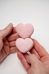 Hands gently holding two heart-shaped pink macarons, representing love, celebration, and delicious sweets perfect for Valentine's Day or a romantic gesture on a clean white background