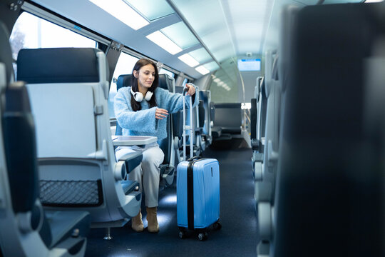 A seated woman with a suitcase in a train, showcasing a blend of comfort, style, and excitement for travel.