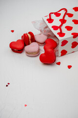 Heart shaped red and pink macarons falling out of a white paper gift bag with red hearts, symbolizing love, romance, and sweet treats for Valentine's Day or an anniversary celebration
