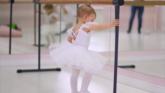 Moscow, Russia,04.04.2024 Little girl in white tutu at ballet barre. Child balerina practicing dance moves in studio. Childhood dance education and hobby concept.