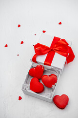 Heart-shaped red macaroons are presenting a sweet gift inside an open white box tied with a red ribbon, celebrating love and romance on a textured white background with confetti