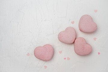 Pink heart macarons and confetti hearts are neatly arranged on a white textured background, creating a sweet and romantic flat lay composition ideal for celebrating love and special occasions