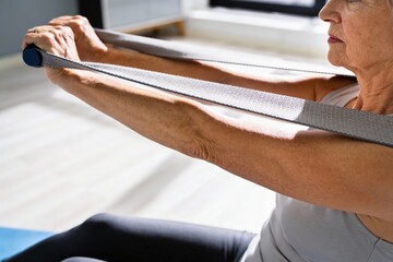 Obraz premium Active senior woman performing strength exercise using a resistance band at home with copy space for healthy aging concept.