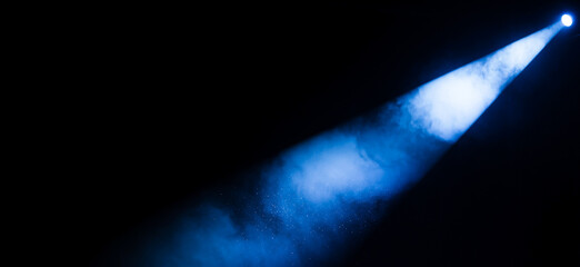 Pitch-black theater with a single white spotlight sweeping across the stage