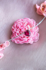 Jewelry. Metal chain with stylish pink heart pendants on soft silk fabric. Rose and petals of rose creating, tender, romantic atmosphere. Valentine's day,  mother's, woman's day, love holidays.