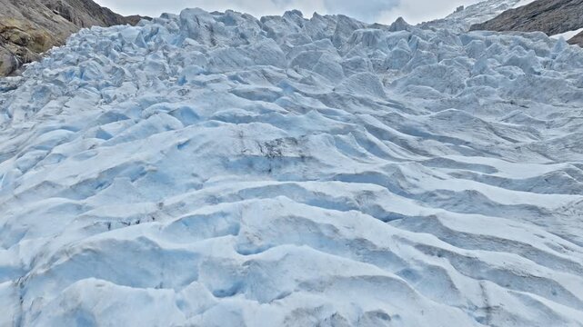 Detailed aerial shot of Briksdalsbreen glacier surface in Norway. Drone captures blue ice patterns and deep crevasses in a powerful summer nature scene.