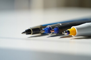 Close up view of several colorful pens neatly lined up on a pristine white surface, highlighting their various nibs and caps