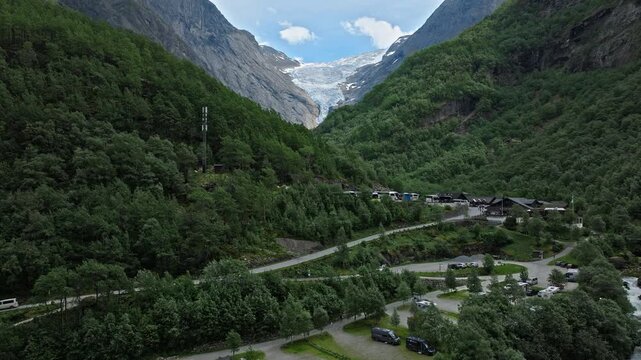 Drone view above Briksdalen valley near Briksdalsbreen, Norway. Forested slopes, roads and distant glacier scenery create a peaceful summer mountain landscape.