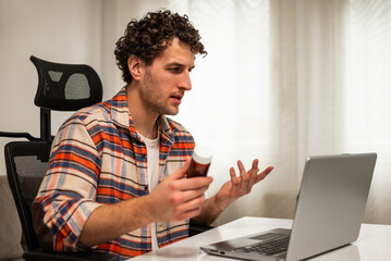 Young man sitting in living room, communicating with healthcare professional via video call on laptop, discussing his medical condition and treatment options. Telemedicine concept.	