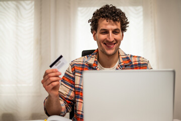 Happy young businessman using laptop and credit card for electronic banking and e-commerce transactions while sitting in comfortable home office.	