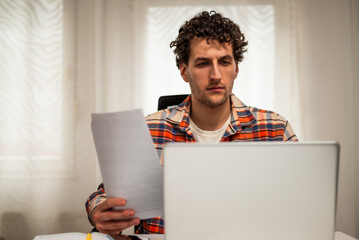 Focused businessman using laptop and examining documents while working from his cozy home.	