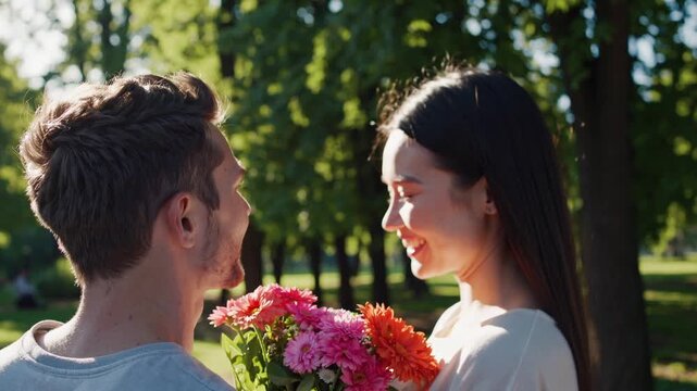 Over the shoulder shot of a young man giving a beautiful bouquet of colorful gerbera daisies to his smiling girlfriend on a sunny day