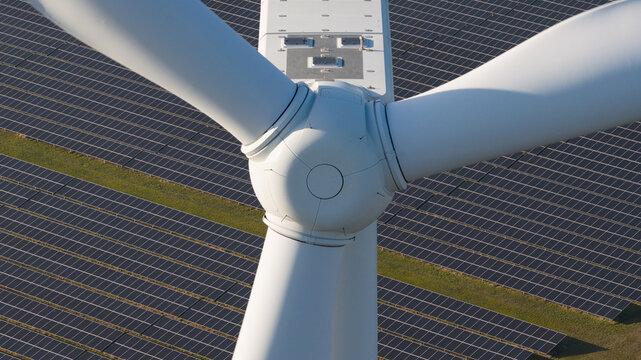 Aerial view of a wind turbine's stark white blades contrasting against the dark solar panels, Middelharnis, South Holland, Netherlands.